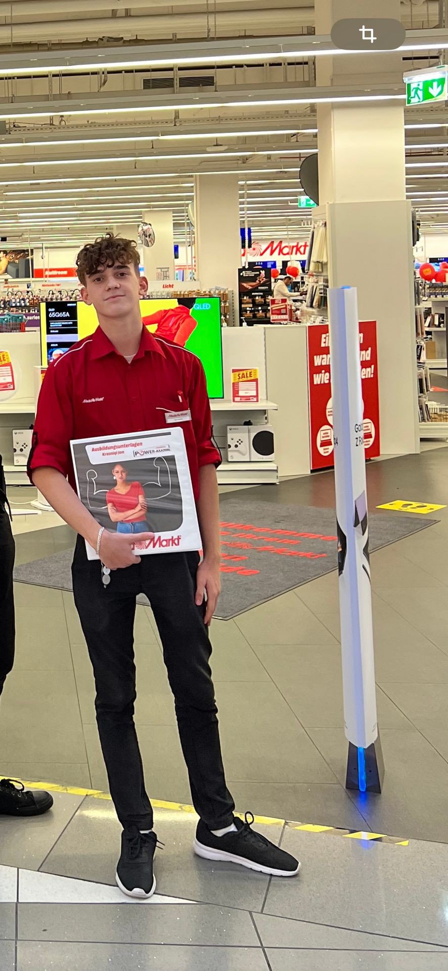 Person in a red shirt holding a folder with product information inside a electronics store.